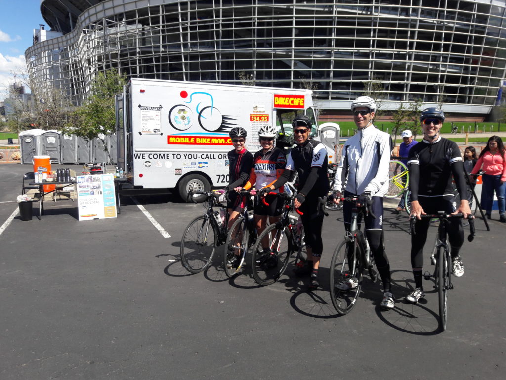 Original Mobile Bike Shop Repair Van with Mile High Stadium in background; foreground shows happy bike expo attendees posing with their bicycles